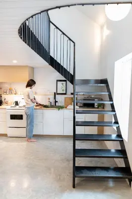 a woman standing in a kitchen next to a spiral staircase at Le Central par Maison Dudley in Lac-Mégantic