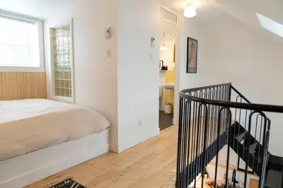 a white bedroom with a bed and a staircase at Le Central par Maison Dudley in Lac-Mégantic