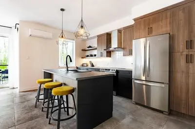 a kitchen with a stainless steel refrigerator and stools at Le Memph Hirondelle spacious comfortable condo cottage eco responsible 3 bedrooms - hot tub & pool Memphrémagog Lake in Magog-Orford