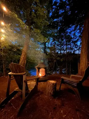 a fire pit with a bench and a chair next to a tree at Le Perché-sur-la-rivière in Joliette