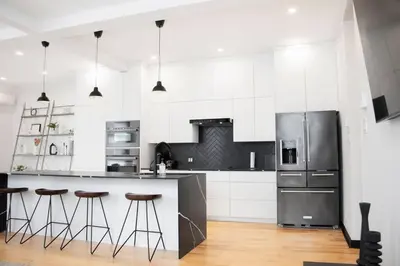 a white kitchen with a refrigerator and bar stools at Upscale 3-Bedroom Entire Unit in the Trendy Plateau Mont-Royal featuring A Magazine-Worthy Kitchen & Opulent Living Spaces - Apt 1 in Montréal