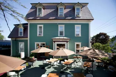 a large green house with tables and umbrellas in front of it at Le Pleasant Hôtel & Café in Sutton
