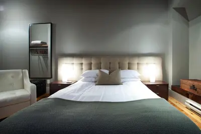a bedroom with a large bed and a chair at Le Pleasant Hôtel & Café in Sutton