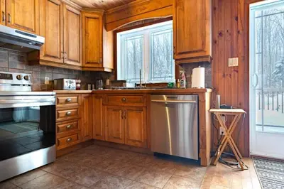 a kitchen with wooden cabinets and a stainless steel refrigerator at Chalet in a dark sky reserve in Notre-Dame-Des-Bois