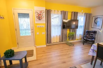a living room with yellow walls and a table and a television at Maisonnette dans la nature en pleine ville. in Trois-Rivières