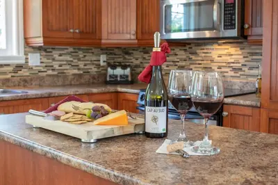 a bottle of wine and two wine glasses on a kitchen counter at Chalet BIA - Cap au Sud in Trois-Lacs