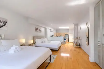 a bedroom with two beds and a kitchen in the background at Loft The White Pearl Plateau-Mont-Royal 3 Beds in Montréal