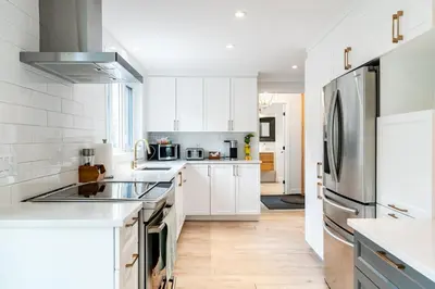 a kitchen with white cabinets and a stainless steel refrigerator at lacbrome Chalet lake+Terrasse+BBQ+Hot-tub in Lac-Brome