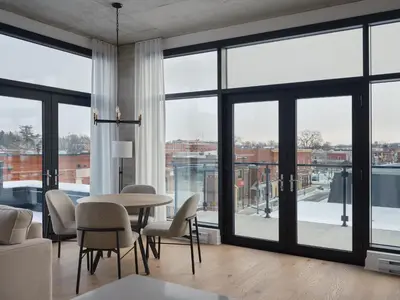 a living room with a table and chairs and large windows at Hôtel Expérience - Quartier Des Marinas in Magog-Orford