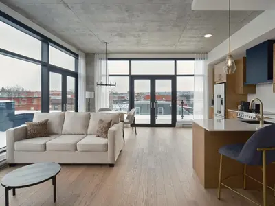 a living room with a white couch and a kitchen at Hôtel Expérience - Quartier Des Marinas in Magog-Orford