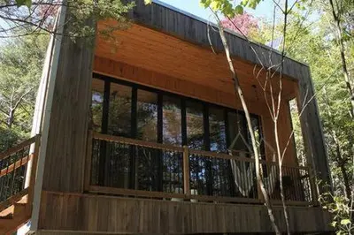 a wooden house with glass windows in the woods at Cabin Zoobox 54 in Eastman