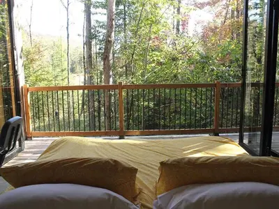 a porch with a bed and a balcony with a fence at Cabin Zoobox 55 in Eastman