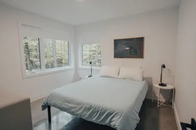 a white bedroom with a bed and two windows at Cottage 42 de la Réserve in Eastman