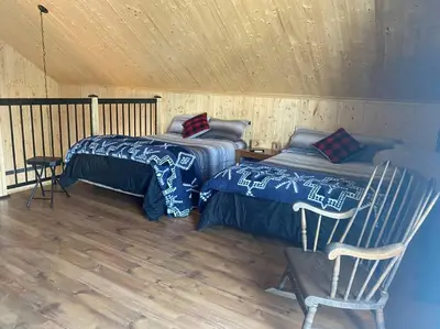 a room with two beds and a chair in a cabin at LE JAZZ- Chalet rustique/chic avec SPA in Notre-Dame-Des-Bois