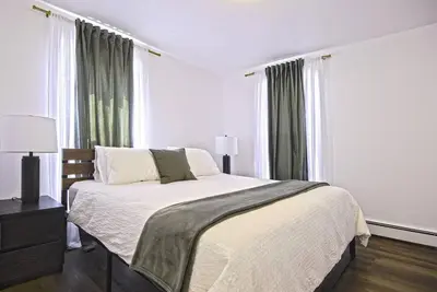 a white bedroom with a bed and two windows at Downtown Prestige: Parking, King Bed, Sleeps 6 in Sherbrooke
