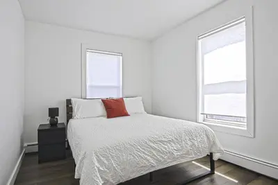 a white bedroom with a bed and two windows at Downtown Prestige: Parking, King Bed, Sleeps 6 in Sherbrooke