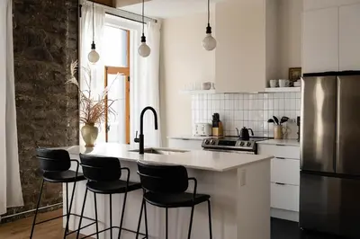 a kitchen with a white counter and black chairs at Maison Place Royale by Luxury In Transit in Montréal