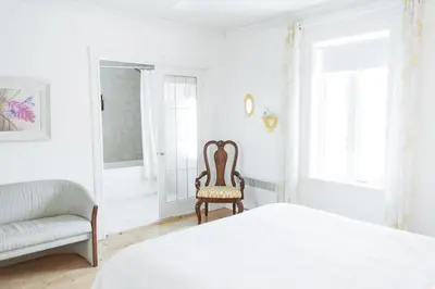 a white bedroom with a chair and a bed at Auberge Incroyable in Saint Adrien