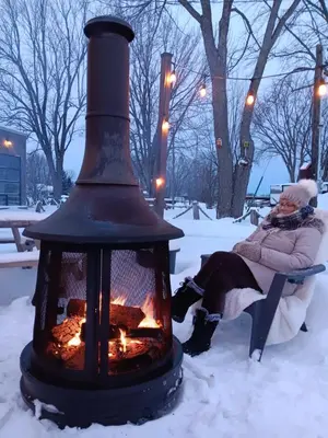 a woman sitting on a bench next to a fire in the snow at Loft in Louiseville
