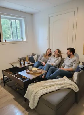 three people sitting on a couch in a living room at Cozy 1BR in Vieux-Longueuil +parking 14min Downtown in Longueuil