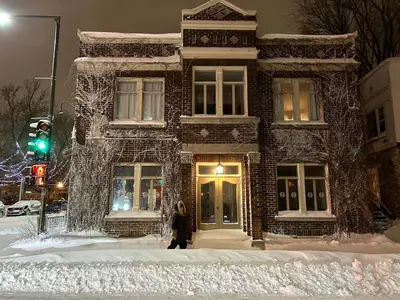 a woman walking in front of a brick building in the snow at Pignon sur Parc in Trois-Rivières