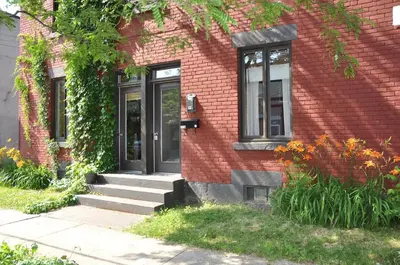 a red brick building with a black door and stairs at Le Tierra del Fuego by HomeInMontreal in Montréal