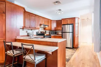 a kitchen with wooden cabinets and a kitchen island with two chairs at Le Metro Mont-Royal by HomeInMontreal in Montréal
