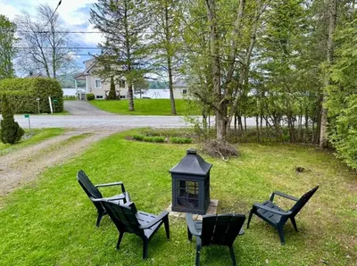 three chairs and a table with a lantern in the grass at Repère d'Eastman - Spa et Accès au lac in Eastman
