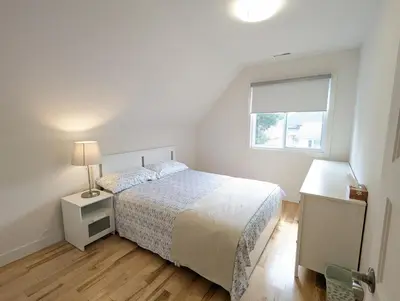 a white bedroom with a bed and a window at Impeccable, modern, river view, renovated cottage in Laval