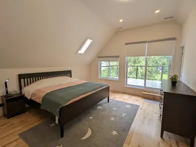 a bedroom with a bed and a desk and windows at Impeccable, modern, river view, renovated cottage in Laval
