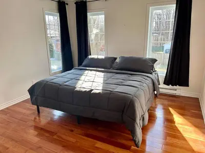 a large bed in a room with two windows at 3BR House 6 Guests Near Water in Laval