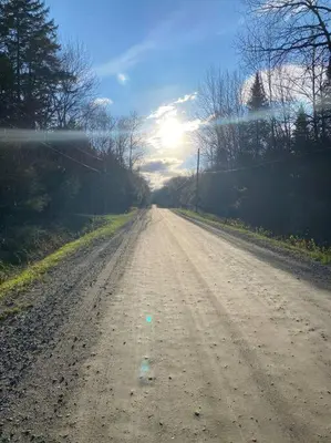 a dirt road with the sun in the distance at Le Highwater - Cabin in Mansonville