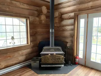 a stove in a log cabin with two windows at Chalet en bois rond des Perséides in Saint-Isidore dʼAuckland