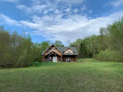 a log house on a grassy field with trees at Chalet en bois rond des Perséides in Saint-Isidore dʼAuckland