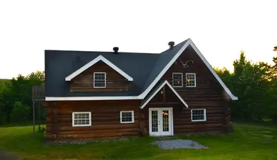 a wooden house with a black roof at Chalet en bois rond des Perséides in Saint-Isidore dʼAuckland
