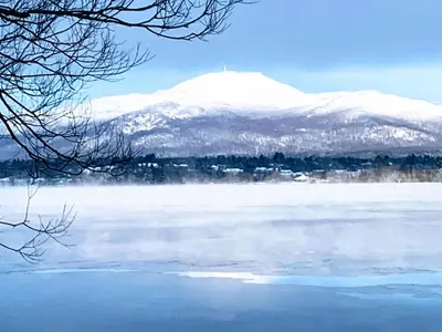a snow covered mountain in front of a body of water at OMagogcondo com A in Magog-Orford