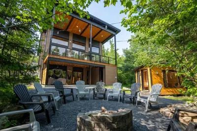 a house in the woods with chairs and a fire pit at Évasion Nature Adstock - Sauna, Ski & Spa in Thetford Mines