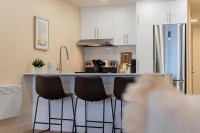 a kitchen with three bar stools in front of a counter at DownTown King Suite with Balcony in Montréal