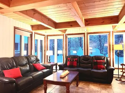 a living room with black leather furniture and windows at Chalet familial et SPA à proximité du Mont Orford in Orford