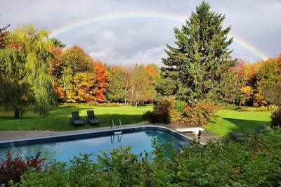 a rainbow over a pool in a yard with trees at L'Orford VIEW POOL TENNIS SPA in Orford