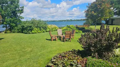 two chairs and a table on a lawn near the water at Hotel Oasis Lac St-Louis in Salaberry de Valleyfield