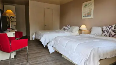 a hotel room with two beds and a red chair at Hotel Oasis Lac St-Louis in Salaberry de Valleyfield