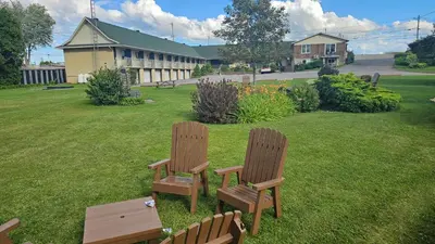 two wooden chairs sitting in the grass near a building at Hotel Oasis Lac St-Louis in Salaberry de Valleyfield