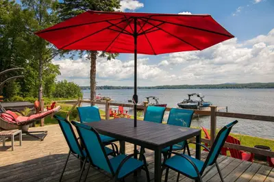 a table with chairs and a red umbrella on a deck at La Cozy O-Lac Magog in Sherbrooke