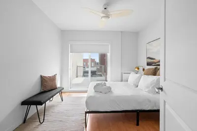 a white bedroom with a bed and a chair at Trendy 2-Bedroom Haven by Jean Talon Market in Montréal