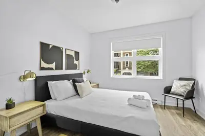 a white bedroom with a large bed and a chair at Stylish 2 Bedroom Haven by Jean Talon Market in Montréal