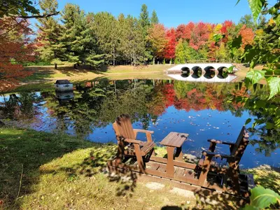 two chairs sitting next to a pond with trees at L'Ile Enchantée in Trois-Rivières