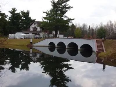 a reflection of a white bridge in a body of water at L'Ile Enchantée in Trois-Rivières