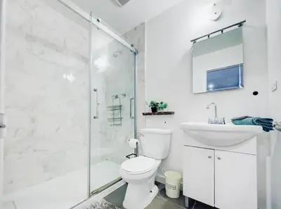 a white bathroom with a shower and a toilet and a sink at Charming 2 BD condo griffintown in Montréal