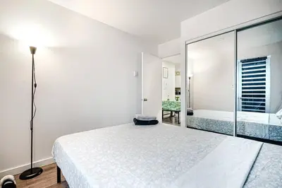 a white bedroom with a bed and a mirror at Bienvenue dans votre havre de paix à Griffintown in Montréal